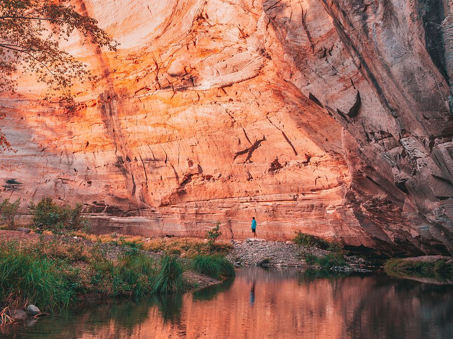 A walker dwarfed by glowing orange sandstone walls above a creek